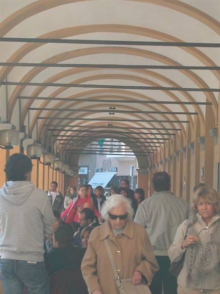 Pedestrian in sunglasses beneath crowded ochre arched colonnade walkway