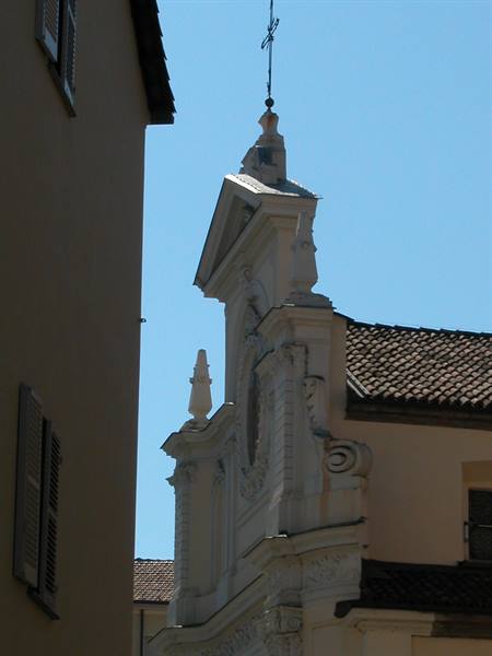 White Baroque church facade with metal cross, between ochre houses