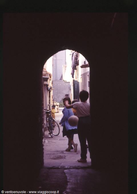 Children with a ball playing in an alley seen through a dark archway