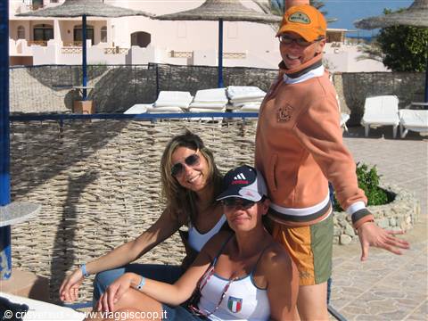 Three smiling tourists in caps beside straw umbrellas and white sun loungers