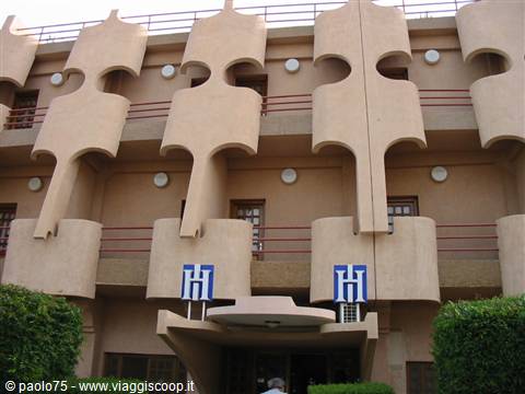 Pink concrete facade with geometric balconies and blue hotel signs