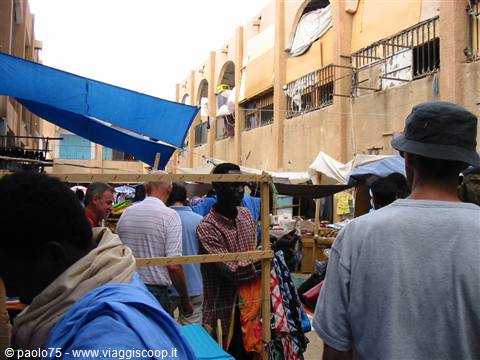 Crowded market among earthen buildings, blue tarps and shade