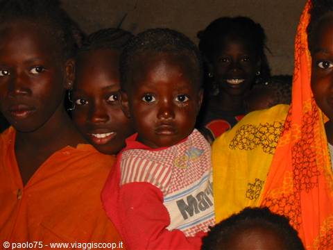 African children together wearing bright orange and yellow clothes inside a dim house