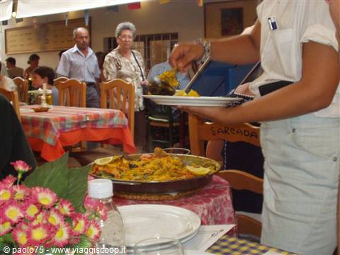 Waiter serving paella from the pan to restaurant tables
