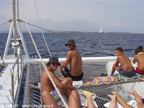 Guys lounging on the catamaran trampoline net, blue sea and sailboat behind
