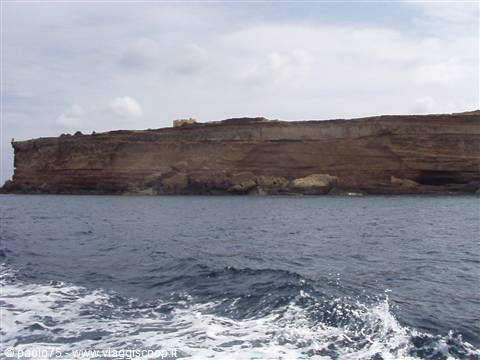 Sedimentary rock cliff seen from the sea, boat wake in foreground
