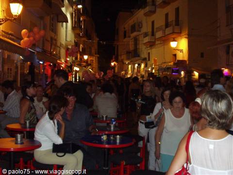 Crowd at outdoor cafés on a city street at night, red tables lit