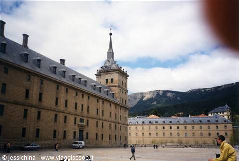 El Escorial monastery, granite facade under clouds, tourists in the square