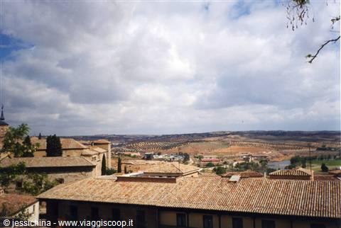 Terracotta tiled rooftops and cultivated hills under clouds in Toledo