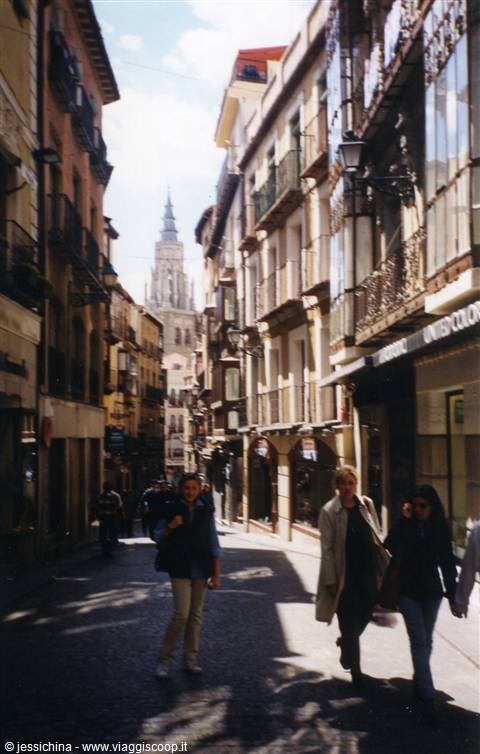 Pedestrians on a Toledo street with the cathedral tower in the background