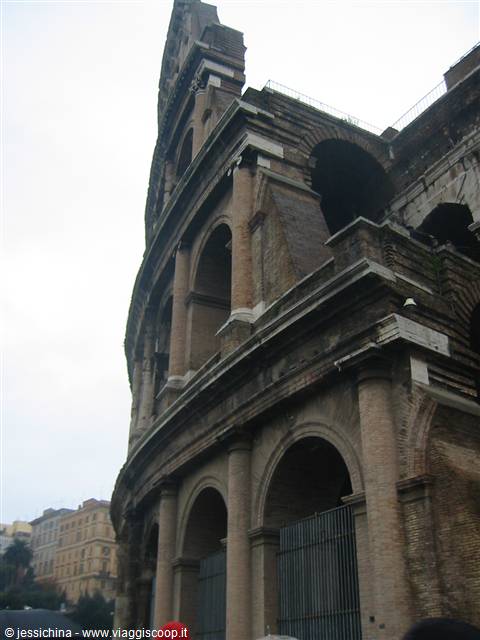 Travertime facade of the Colosseum with arches and gates, grey sky