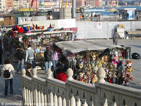 Venetian carnival mask stalls by the waterfront, shoppers browsing under bright daylight