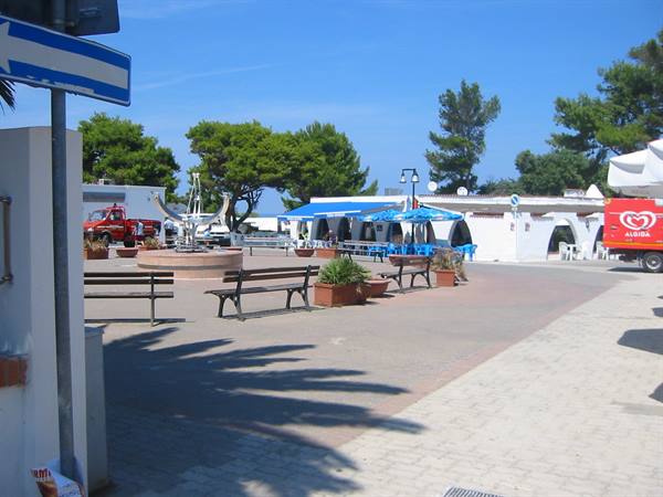 Small square with benches and fountain, blue umbrellas in front of kiosks