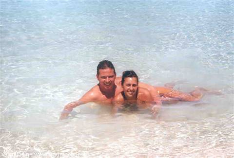 Couple swimming and laughing in clear turquoise water over white sand