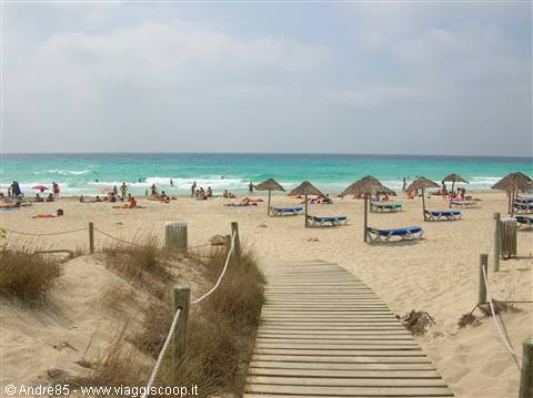 Wooden boardwalk over dunes leads to beach with straw umbrellas and turquoise sea