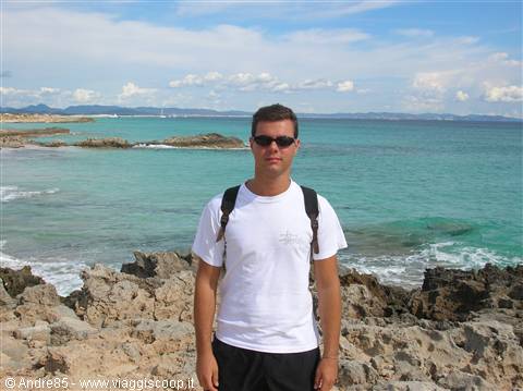 Young man with backpack and white T-shirt on rocks by turquoise sea
