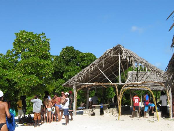 Tourists and locals under a thatched beach hut on white sand