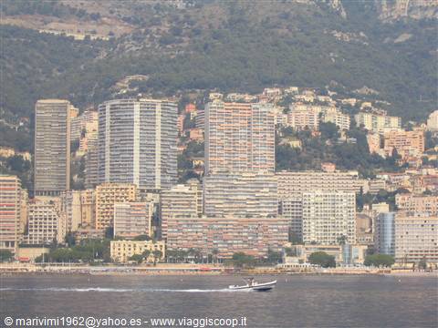 Motorboat speeding past Monaco's waterfront high-rise buildings on a hazy day