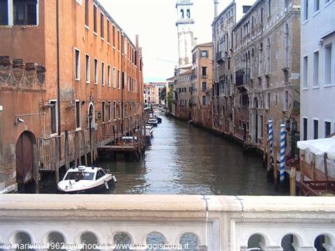 Venice canal with ochre buildings, moored boat and bell tower beyond