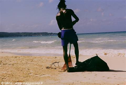 Man with rake and black bag cleans the beach under the sun