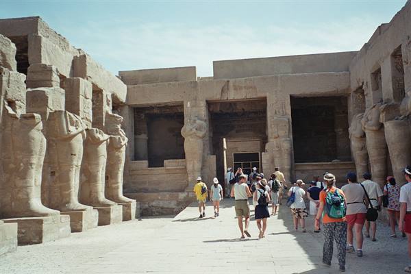 Tourists walk toward the pylon of Medinet Habu temple among sandstone pharaoh statues