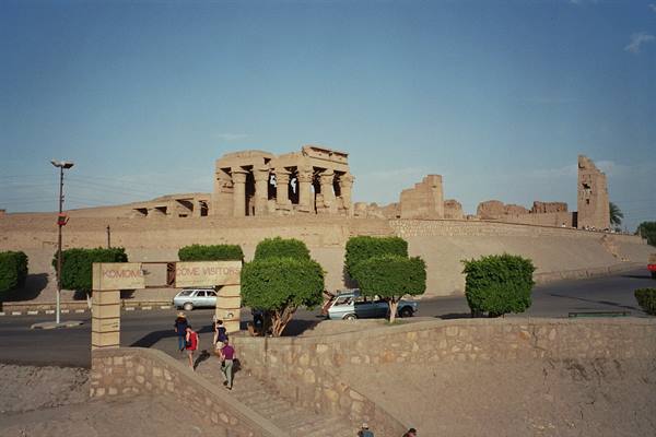 Tourists climb toward Kom Ombo temple, sandstone ruins under afternoon light