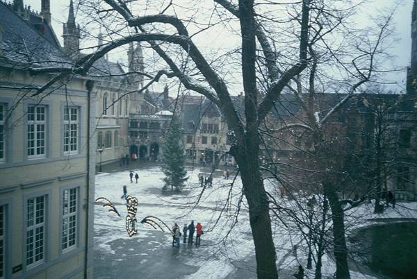 Snowy square in Bruges with Christmas tree and people among historic buildings