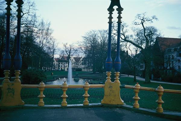 Fountain in park pond seen from pavilion with blue and yellow columns