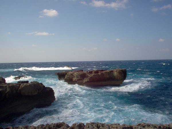 Waves crashing on limestone rocks under a blue sky
