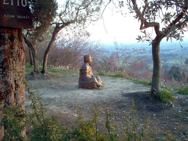 Seated monk statue meditating among trees on hill overlooking valley