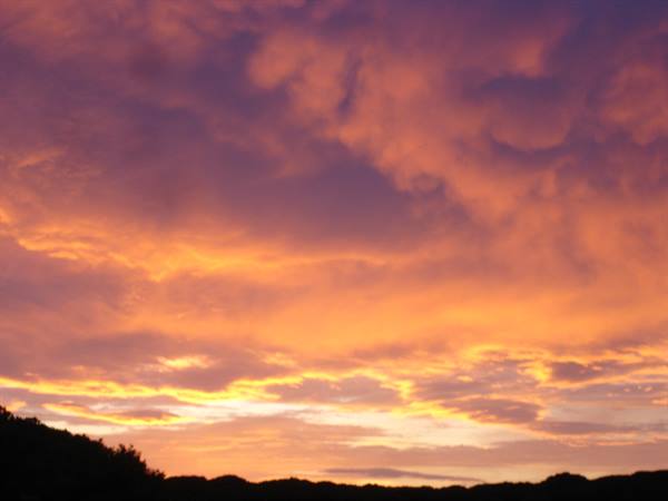 Orange and purple clouds at dusk over a dark hill silhouette
