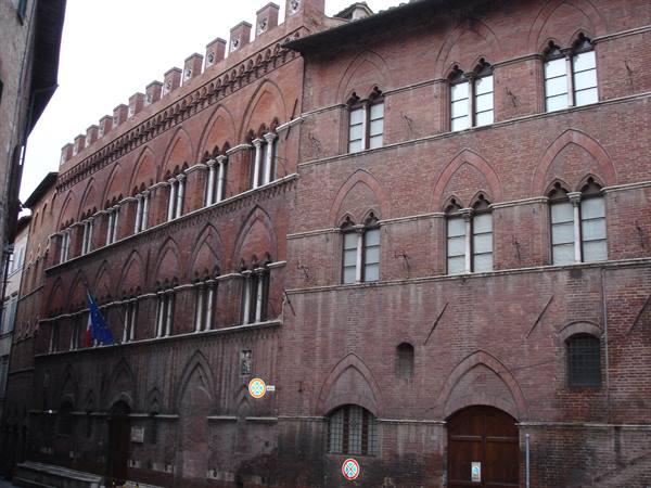 Red brick Gothic palace with mullioned windows and flags in Siena