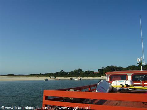 Red boat sailing toward sandy beach with anchored boats