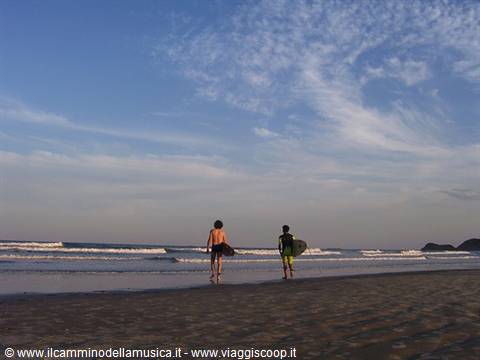 Two surfers carrying a board walk into the ocean waves on the beach