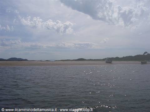 Boat on sea in front of sandy beach, hills under cloudy sky