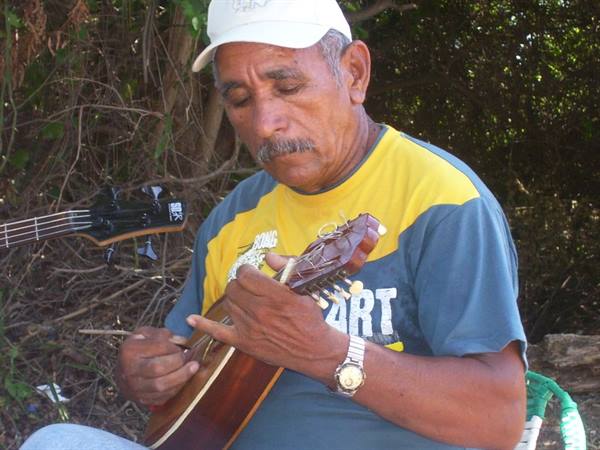 Man in white cap playing a small guitar among green trees