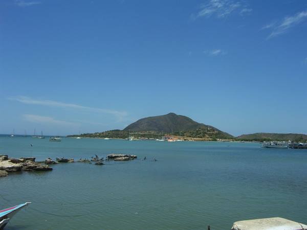 Colorful boat on turquoise sea, rocks and green hill under blue sky