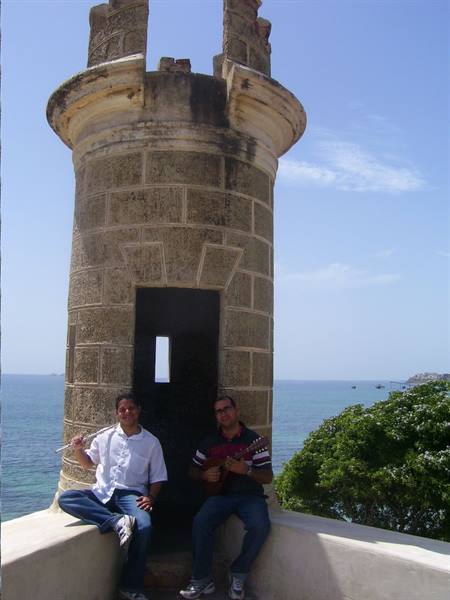 Two men seated in front of a stone tower by the sea