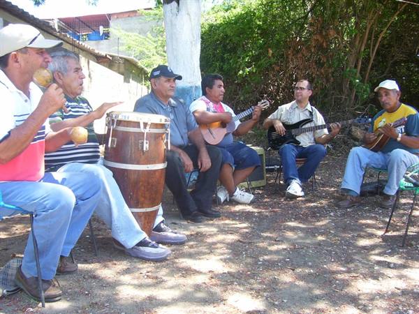 Musicians in the shade play drum, guitars and maracas seated outdoors