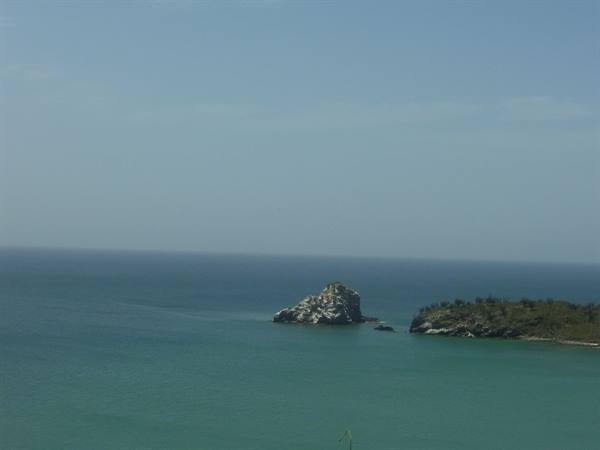 Rocky islet in turquoise sea, hazy sky
