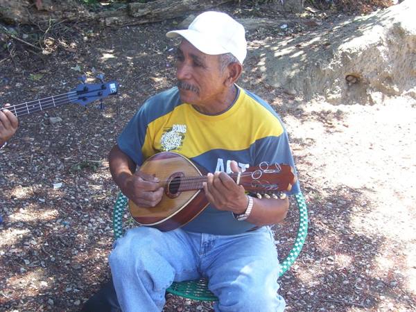 Man in white cap plays a wooden mandolin beside a bass player
