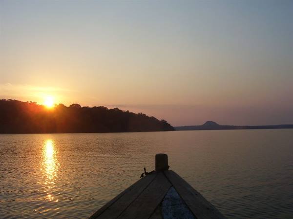 Wooden boat bow on the lake at sunrise, silhouetted trees ahead