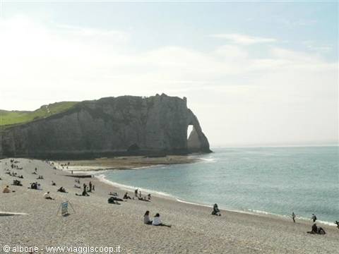 Tourists on pebble beach beneath the limestone cliff and natural arch of Étretat