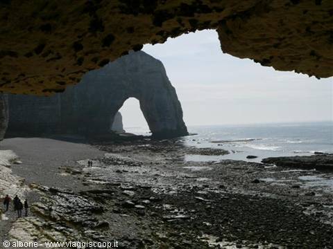 Étretat natural arch seen through another arch, tourists on pebble beach