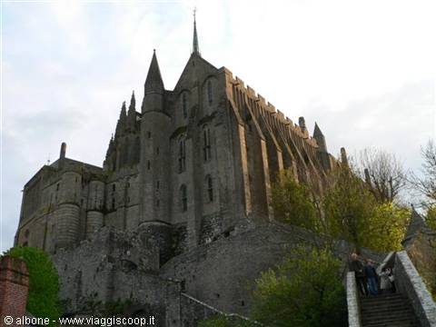 Mont-Saint-Michel abbey, stone walls under cloudy sky, visitors on the stairs