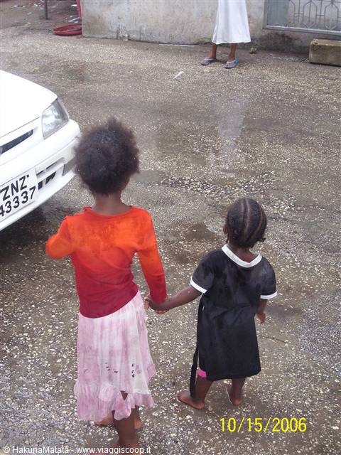 Two little girls holding hands on a wet street, white car with Zanzibar plate
