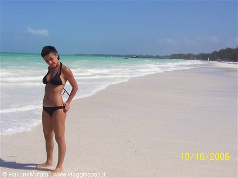 Woman in black bikini on white sand beach, turquoise water, gentle waves