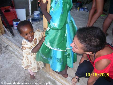 Smiling toddler next to a girl in a green dress, tourist crouching on the sand
