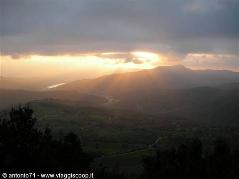 Sunrays breaking through clouds over green hills and a lake