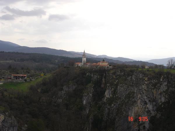 Village church tower on a rocky cliff among wooded hills